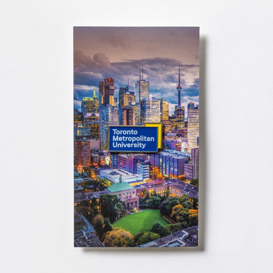 Mounted on cardstock featuring an artist's rendering of the Toronto Metropolitan University campus & Toronto, this soft enamel lapel pin is the perfect addition to your TMU wardrobe. The pin is 1.25" wide