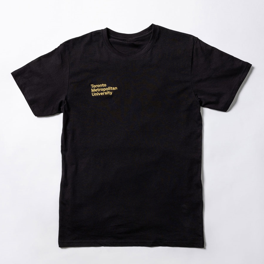 A short-sleeved black t-shirt features a printed "Toronto Metropolitan University" small stacked wordmark logo on the front right chest in embroidered metallic gold.